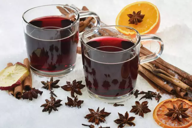 Two glasses of mulled wine surrounded by a decoration of spices such as cinnamon, cardamom and orange slices.